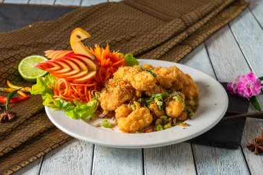 Lezzetli bir tabakta lezzetli kızarmış deniz ürünleri, canlı sebze süsleri ve taze limonla güzelce düzenlenmiş. Tabak, görsel cazibesini arttırmak için kırsal bir masa örtüsüne kurulmuş..