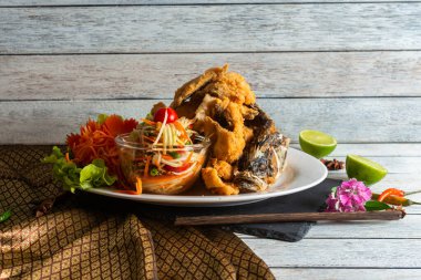 Limon ve dekoratif çiçeklerle süslenmiş taze sebze ve bitkilerden oluşan canlı bir salatanın yanında kızarmış balık. Kompozisyon harika bir aşçılık deneyimi sergiliyor..