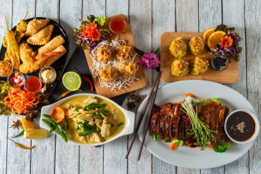 Canlı Asya yemekleri kırsal ahşap bir masayı süslüyor. Izgara proteinler, karışık aperatifler ve renkli garnitürler duyular için bir ziyafet yaratıp herkesi her lezzetin tadına varmaya davet ediyor..