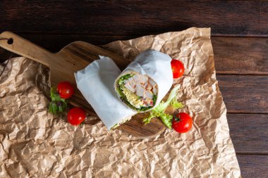Taze sebzeler ve ızgara tavukla dolu bir sargıyla çevrili ahşap bir tahtada sunulmuş canlı domateslerle dolu bir mutfak lezzeti..