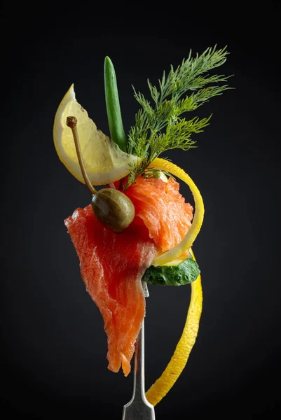 Salmon slices on a fork. Smoked salmon with dill, cucumber, capers, green onion, and lemon slice.