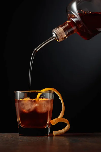 Old-fashioned cocktail with ice and orange peel. Whiskey is poured into a glass with ice.