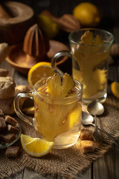 Ginger tea with lemon and brown sugar in a glass cup on an old wooden board in rustic style.