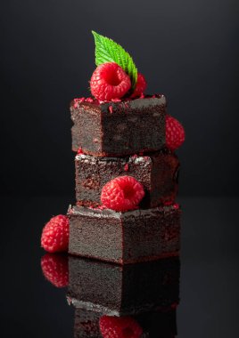 Chocolate cake garnished with fresh raspberries on a black reflective background.
