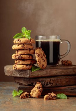 Freshly baked chocolate cookies with mint and a cup of black coffee on a rustic brown background.