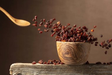 Kahverengi arka planda uçan kuru üzümler. Tahta bir kasede kuru üzümler. Boşluğu kopyala.