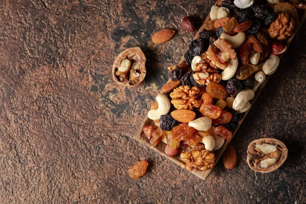 Mix of nuts and raisins on a brown rustic background. Presented raisins, walnuts, hazelnuts, cashews, pecans, and almonds. Top view.