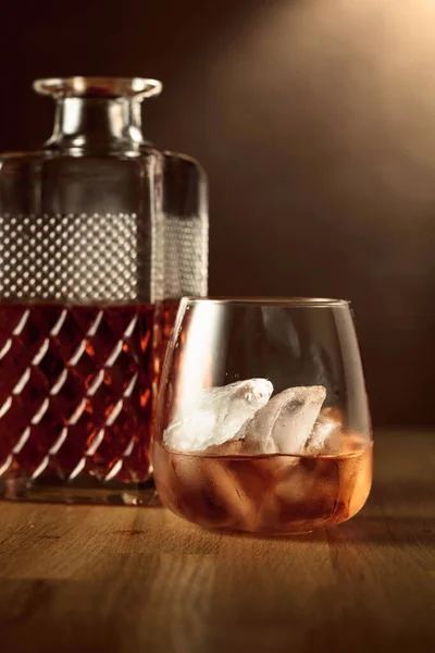 stock image Glass of whiskey with ice on an oak table. Selective focus.