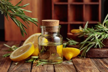 Eski ahşap bir masada bir şişe gerekli yağ, biberiye ve limon. Doğal organik spa malzemeleri.. 