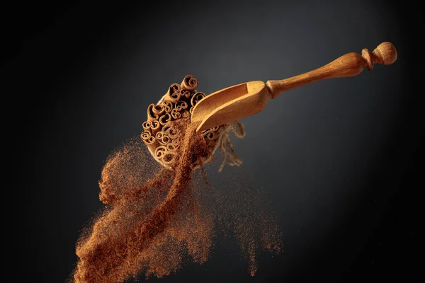 肉桂粉是从木勺里倒出来的 肉桂和肉桂根 用黄麻绳绑在黑色的背景上 — 图库照片
