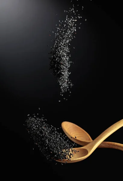 Grains of black sesame are poured with wooden spoons. Black sesame on a dark background. Copy space.