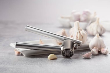 Garlic and garlic press on a grey stone table.