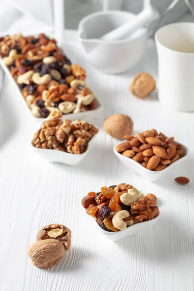 Mix of nuts and raisins on a white wooden table. Presented raisins, walnuts, hazelnuts, cashews, pecans, and almonds.