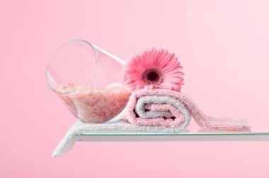 Pembe arkaplanda pembe tuz, gerber ve havlu içeren spa kompozisyonu.