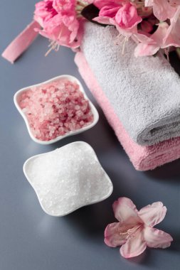 Pembe ve beyaz deniz tuzu, çiçek ve havluyla spa kompozisyonu.