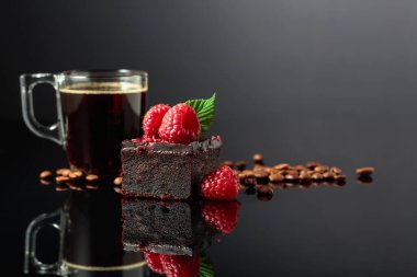 Chocolate cake with fresh raspberries and black coffee on a black reflective background.