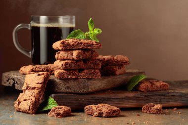 Pieces of fresh brownie with mint and a cup of black coffee on a rustic brown background.