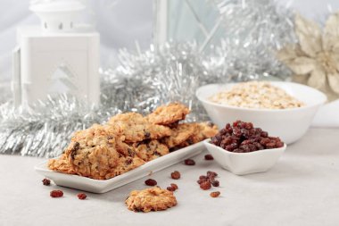 Ev yapımı yulaf ezmeli kurabiye ve Noel süslemeleri olan bir masada kuru üzüm..
