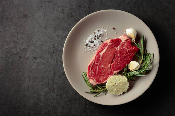 Raw beef meat steak for grilling with rosemary, garlic, salt, and pepper. Top view.