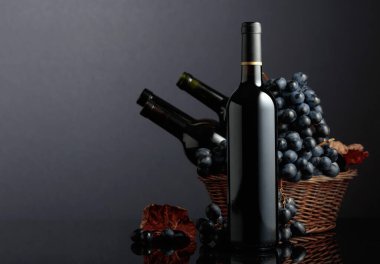 Red wine and blue grapes on a black reflective background. Focus on a bottle.