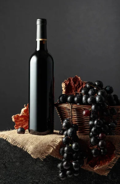 Juicy blue grapes and a bottle of red wine on a black background.