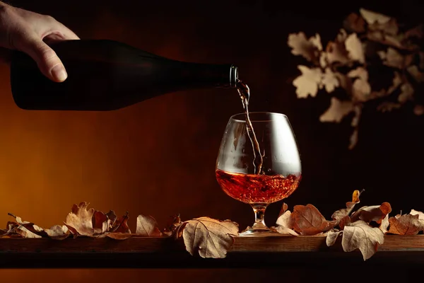 브랜디를 병에서 붓습니다 테이블에 브랜디 냄새마른 나뭇잎 — 스톡 사진