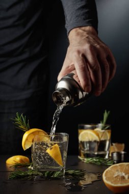 Limonlu ve biberiyeli kokteyl cin toniği. Barmen bardaktan bardağa kokteyl doldurur..