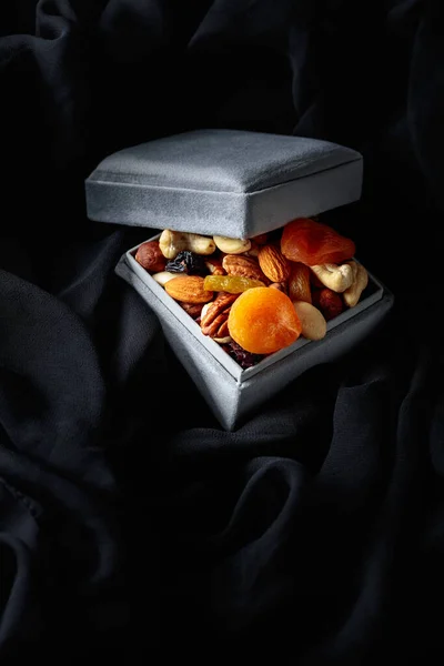Dried fruits and nuts in a gift box on a black cloth.