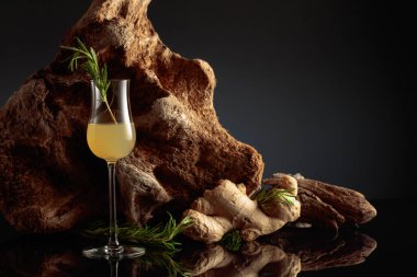 Ginger liquor with a rosemary branch on a black background with an old snag.