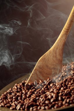 Orta pişmiş kahve çekirdekleri kızartma tavasında dumanlıdır. Boşluğu kopyala.