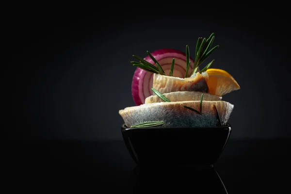 用柠檬 红洋葱和迷迭香加油的鲱鱼片 带鲱鱼的黑色盘子 背景为黑色反光 复制空间 — 图库照片