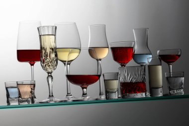 Various alcoholic drinks in a bar on a tilted glass shelf.