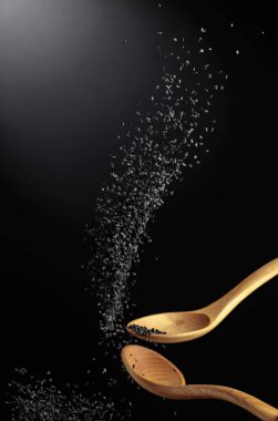 Tahta kaşıklarla siyah susam taneleri dökülür. Karanlık bir arka planda siyah susam. Boşluğu kopyala.