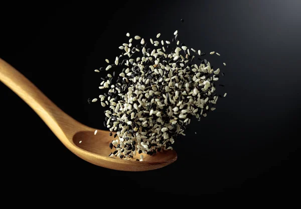 Grains of white and black sesame are poured with a wooden spoon. Black sesame on a dark background. Copy space.