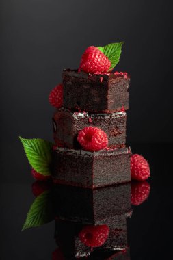 Chocolate cake garnished with fresh raspberries on a black reflective background.
