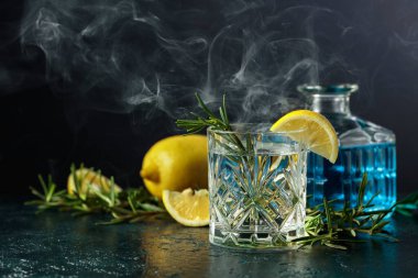 Kristal bardakta limon ve biberiyeli kokteyl cin toniği. Masada tütsülenmiş biberiye eski moda kokteyl..