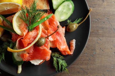 Sandwich with salmon, cream cheese, dill, cucumber, capers, green onion, and lemon. Top view.