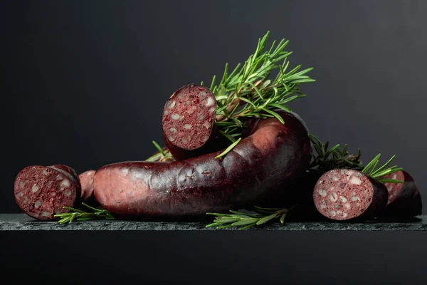 Spanish black pudding or blood sausage with rosemary on a black background.