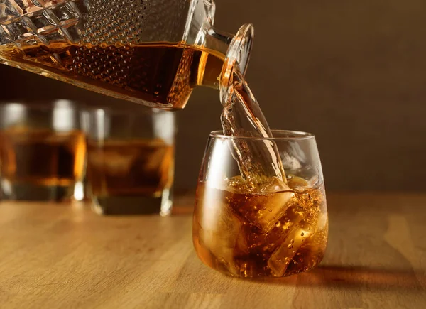 Whiskey is poured into a dammed glass with natural ice. Glass of whiskey on an oak table.