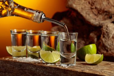 Tequila is poured from a bottle into a glass. Tequila with salt and lime slices on a background of sunset.