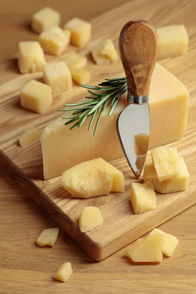 Parmesan cheese with rosemary and knife on a wooden cutting board.