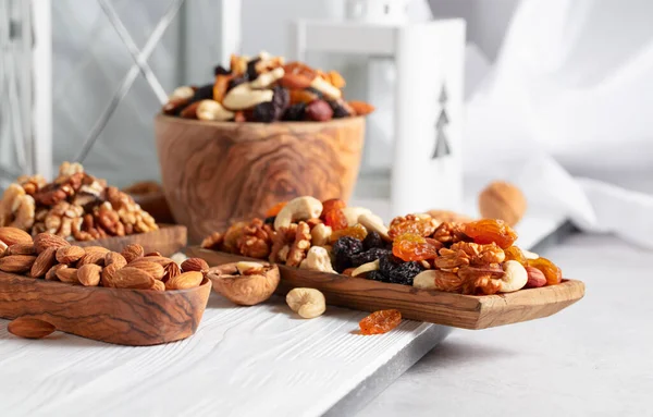 Mix of nuts and raisins on a white wooden table. Presented raisins, walnuts, hazelnuts, cashews, pecans, and almonds.