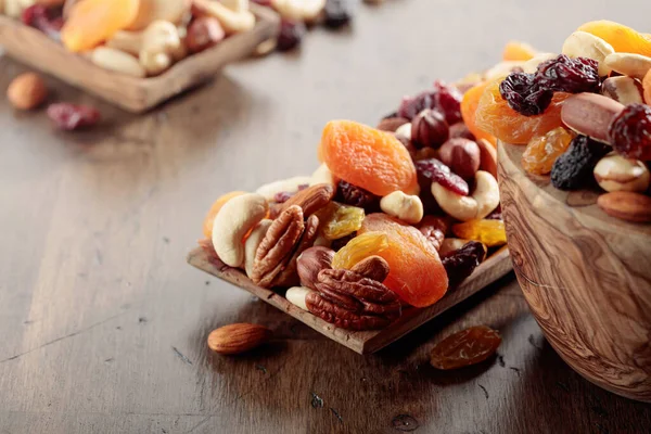 Mix of nuts and dried fruits on an old wooden table. Presented apricots, raisins, walnuts, hazelnuts, cashews, pecans, and almonds. Selective focus.