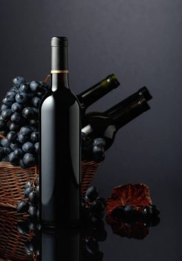 Red wine and blue grapes on a black reflective background. Focus on a bottle.