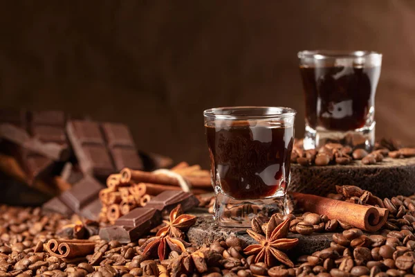 Coffee liquor on a brown background. Coffee beans, cinnamon, anise, and pieces of bitter chocolate are scattered on the table.