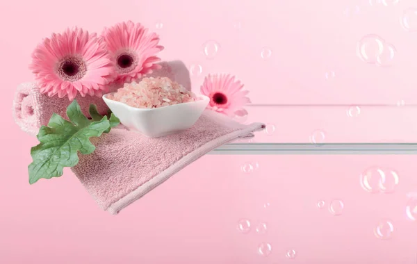 Spa composition with sea salt, pink gerberas, and towels on a pink background with bubbles. Copy space.