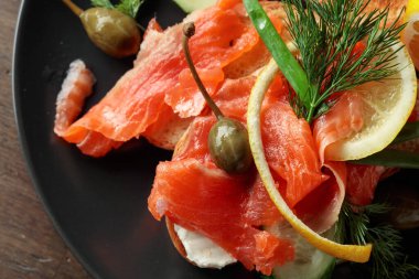 Sandwich with salmon, cream cheese, dill, cucumber, capers, green onion, and lemon. Top view.