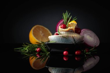 Limonlu balık fileto, kırmızı soğan ve kızılcıkla süslenmiş biberiye. Siyah yansıtıcı arka planda ringa balığı olan siyah bir tabak..