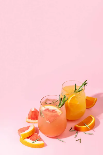 Summer cocktails with grapefruit, orange, rosemary, and ice. Drinks on pink background with copy space. Summer, tropical, fresh cocktail concept.
