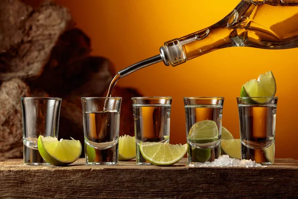 テキラは瓶からグラスに注ぐ 古い板の上に塩とライムのスライスと強いアルコール飲料 — ストック写真